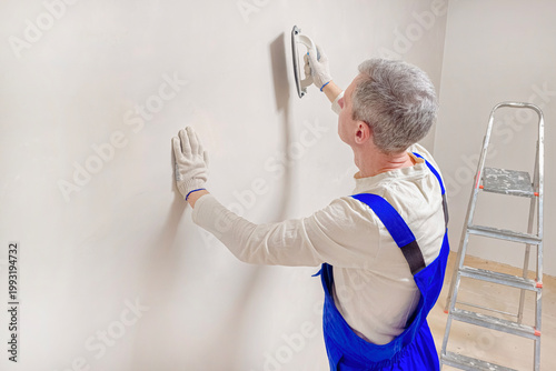 A man applies plaster to a smooth wall using a trowel.