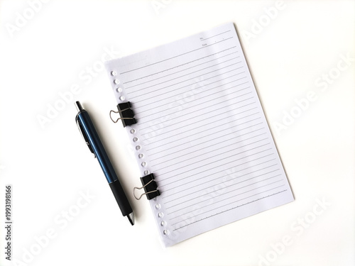 Lined paper with a binder clip attached sits on a white surface. Beside it, a ballpoint pen with a metallic blue and black handle is placed. 