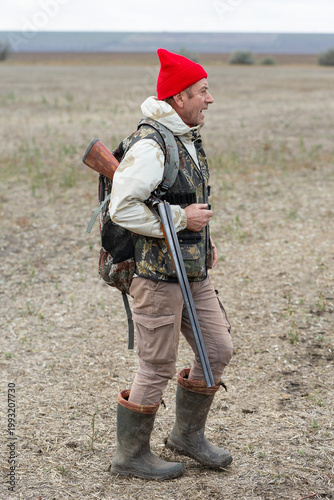A hunter with a gun in camouflage clothing. A senior man with a gun, medium shot, searching for game.