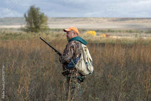 A hunter with a gun in camouflage clothing. A senior man with a gun, medium shot, searching for game.