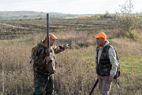 A hunters in camouflage clothing with a gun in his hands walks along the reeds.