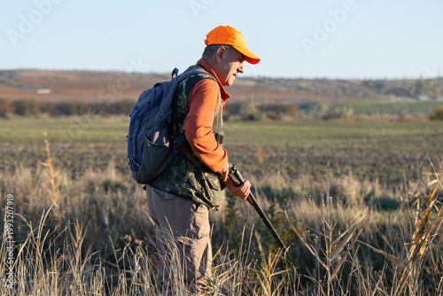 A hunter with a gun in camouflage clothing. A senior man with a gun, medium shot, searching for game.