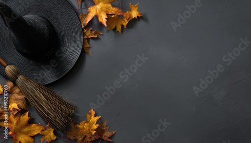 A Black Witch Hat and Broomstick Lie on a Dark Gray Background Scattered with Autumn Maple Leaves and Small Red Beads Creating a Halloween Themed Composition with Glittering Details