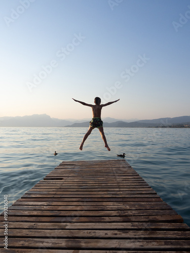 Foto Young boy jumping from wooden pier into lake at sunset, back view of child havin