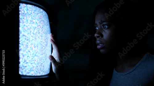 A young woman watches static on an old television screen in a dark room.