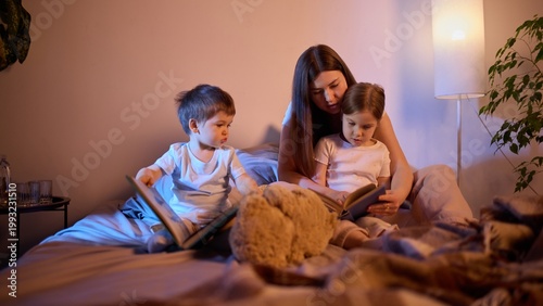 Canvas Print Mother reading books with children on bed in warm evening light