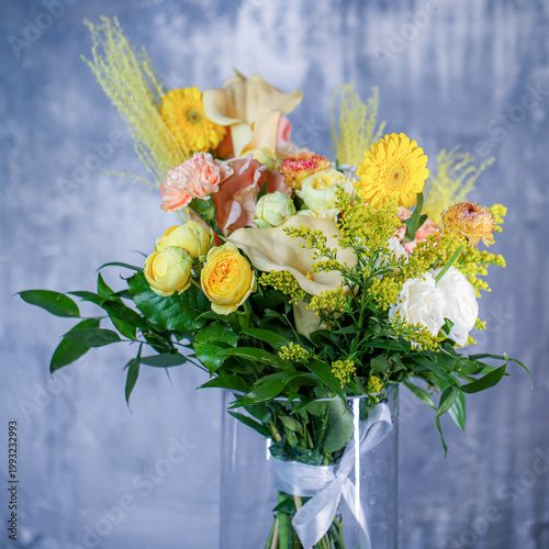 Fotografie Colorful flower bouquet in a clear glass vase on a gray background
