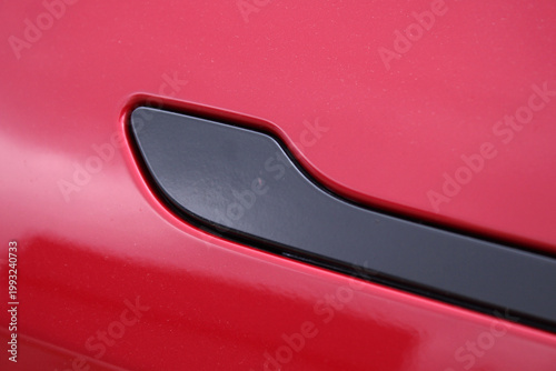 Сlose-up matte black door handle on glossy red car body. Retractable door handle modern electric car. Hidden electric car door handle. Car door handles retracting into body of vehicle close up.
