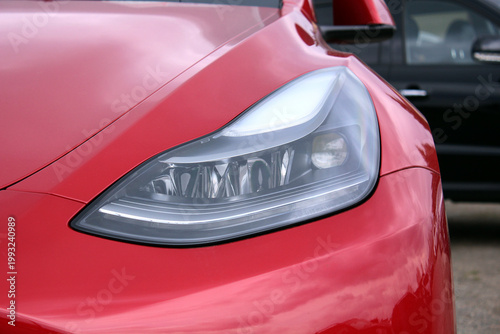Car headlight. Сlose-up of an electric cars headlight. Сlose-up of the cars glossy red headlight cluster. The sleek, thin LED strip of daytime running lights, the projector lens with chrome accents.