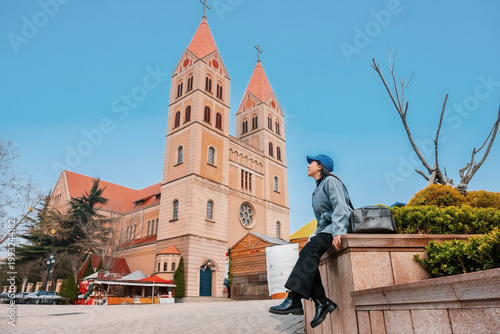 Asian women tourist with cityscape of Qingdao with St. Michael’s Cathedral in China Shandong Province.
