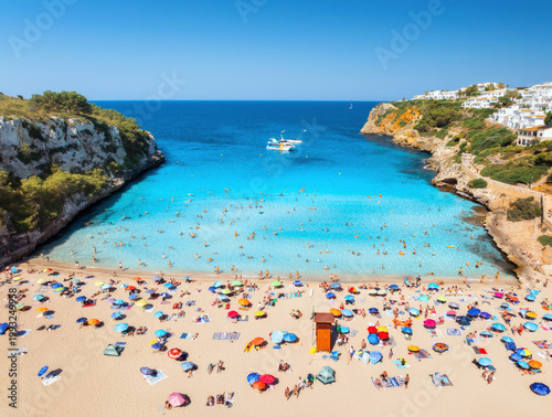 Bild auf Leinwand Aerial view of colorful umbrellas on crowded sandy beach, boats, hotel, rocks, swimmers in blue sea, green trees on sunny summer day