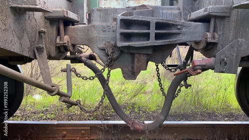 Close-up of a railway automatic coupler connecting two freight cars. Static shot with the chain moving slightly in the wind. Concept of railway transport, logistics and industrial infrastructure. 4K