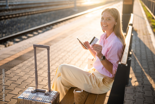 Businesswoman waiting at the train station, using smart phone for online shopping and mobile payment, holding credit card, ready for business travel journey.