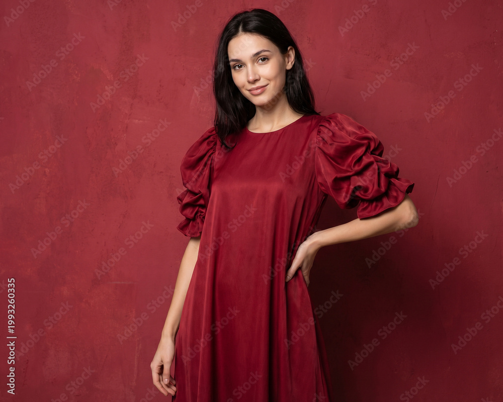 Fototapeta premium Young beautiful slender woman in a fashionable red dress with lush sleeves. Woman posing on a red background