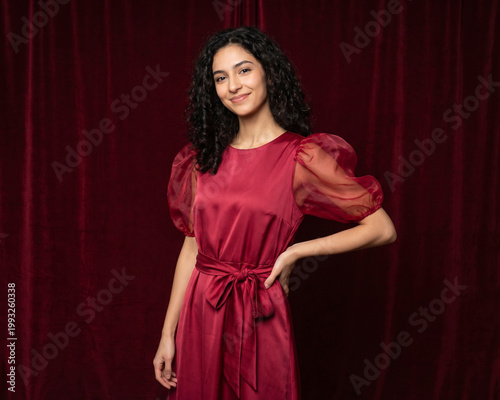 Young beautiful slender woman in a fashionable red dress with lush sleeves. Woman posing on a red background