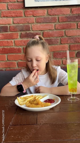 A schoolgirl is eating French fries and chicken nuggets at a cafe restaurant. Junk food for children
