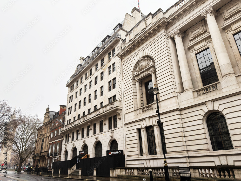 Fototapeta premium Historic neoclassical government building facade in London, UK with pedestrians and umbrellas on rainy street