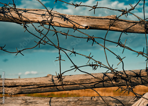 Foto Barbed wire on wooden fence against blue sky and open field in rural area during