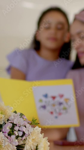 Vertical video: Refocusing camera, daughter in lilac reading Mother's Day card at table, bouquet