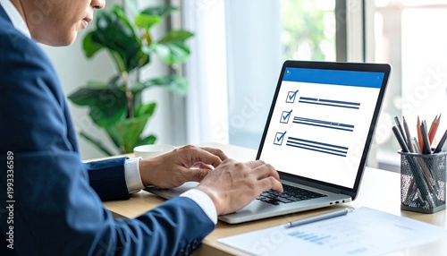 Man in suit types on laptop with checklist displayed on screen, documents on desk