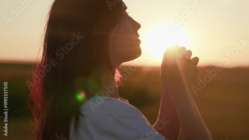Young girl prays against sunny sky, caring for family children. Faith in God. Close-up Christian woman praying at sunrise. Relaxation meditation in nature. Apology. Hope. Life. Free man. Silhouette.