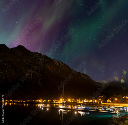 A bautiful aurora borealis display over boats in Norddal village harbor. A spectacular winter night scenery of Norway.