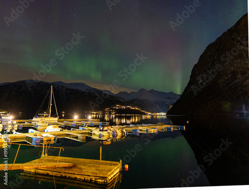A bautiful aurora borealis display over boats in Norddal village harbor. A spectacular winter night scenery of Norway.