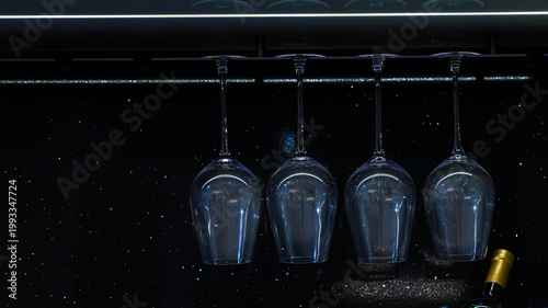 Elegant upside-down wine glasses hanging in a dark bar with sparkling dust, creating a dramatic, modern, and luxurious nightlife atmosphere scene