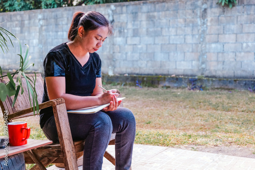 Young Asian Woman Writing in Notebook Outdoors