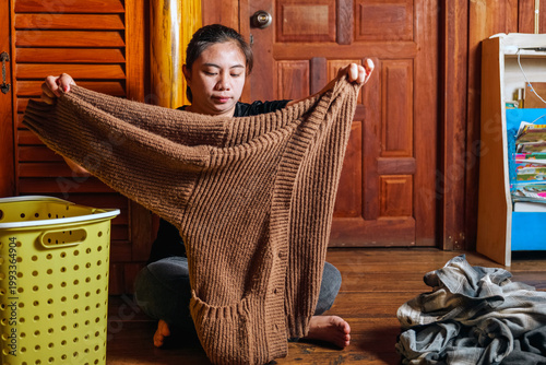 Asian Woman Folding Clothes on Wooden Floor with Laundry Basket