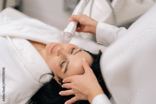 Slika na platnu Close-up top view of relaxed woman receiving innovative rf microneedling facelift procedure from skilled esthetician, modern hardware cosmetology method for skin tightening and wrinkle reduction