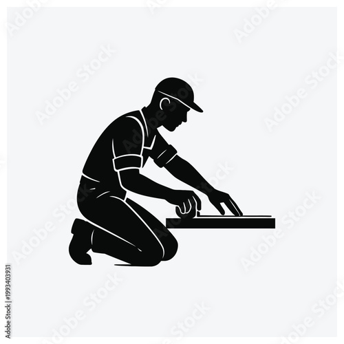 A silhouette illustration of a worker or craftsman kneeling and working on a surface.