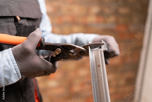 Photos Construction worker using metal shears snips cut of galvanized steel from drywall profile