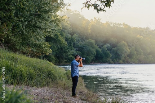 Person With Camera Stands by River During Morning Light Capturing Nature