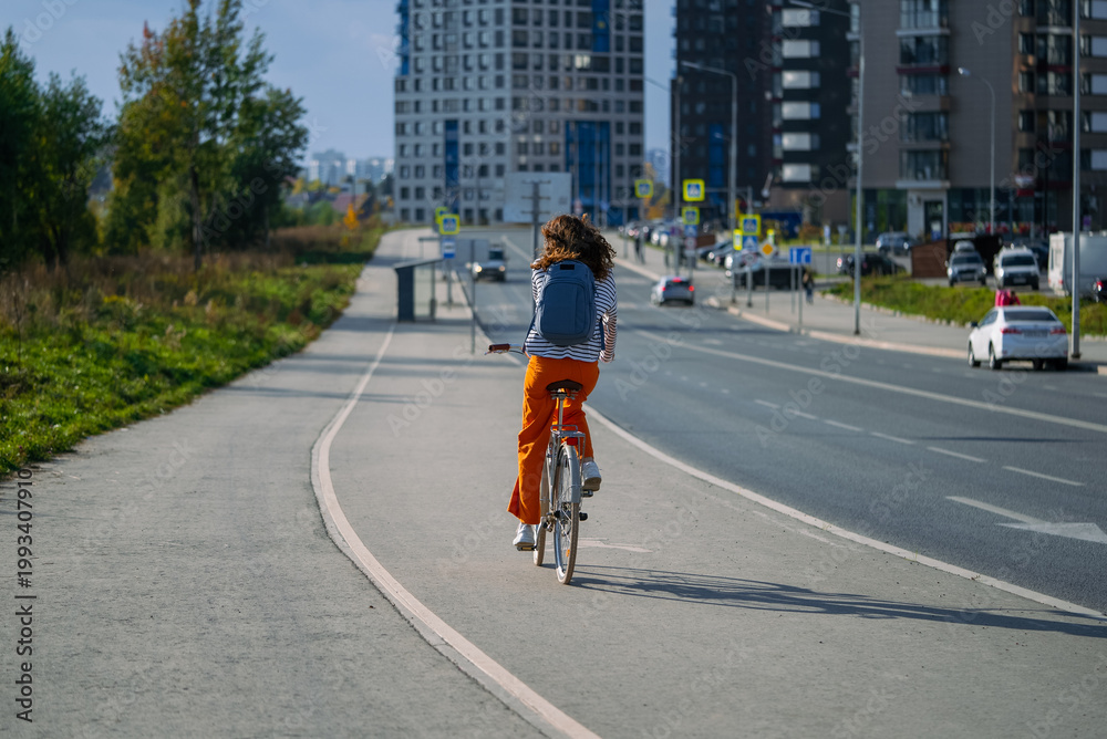 Fototapeta premium Young woman enjoying active healthy lifestyle, riding bicycle on dedicated bike path in modern city, promoting sustainable urban transportation and eco-friendly commute