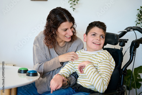 Fotografie Mother supporting son with cerebral palsy using communication buttons