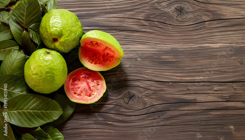 Fresh guavas with red pulp and leaves on a rustic wooden surface. Space for text.