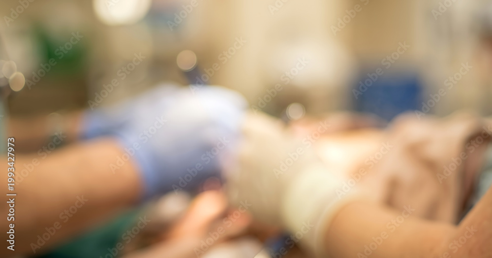Obraz premium A blurred view of a medical procedure showing hands in gloves assisting a patient, emphasizing the clinical environment and teamwork in healthcare.
