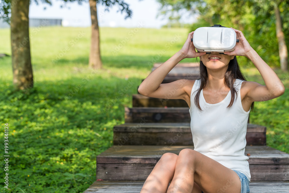 Fototapeta premium Young woman enjoying vr experience sitting in green park