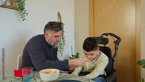 Caring father feeding disabled son in wheelchair at home