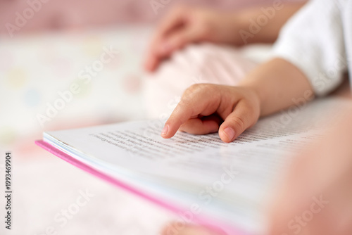 Baby's hand indicating text in a pink book, learning to read with a parent, focusing on early education and literacy