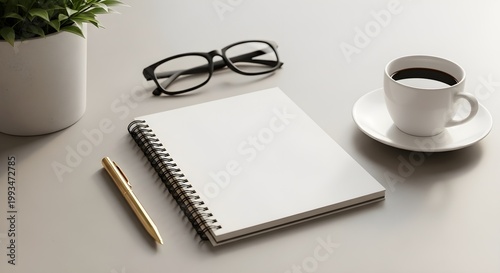 Workspace with a blank spiral notebook, golden pen, glasses, plant, and coffee cup on a light grey desk