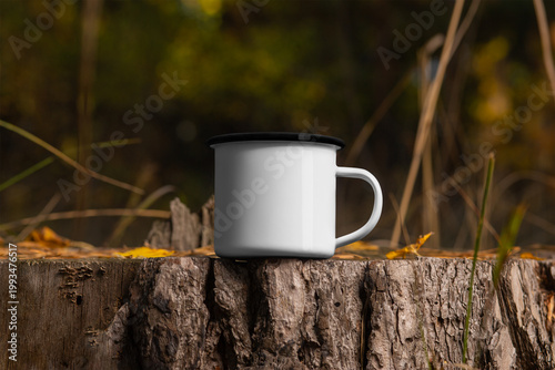 Mockup enamel white mug with black rim on stump, on background nature, product photo outdoors.
