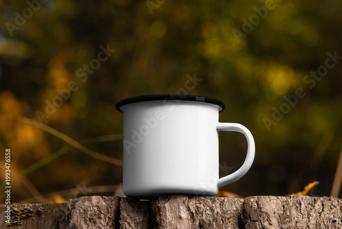 Template of a white iron mug with a black rim on a stump, on a background of nature, outdoors.