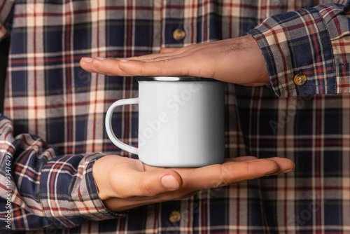 Mockup of a white enamel mug with a rim in hands in a plaid shirt, a steel cup for hot drinks, coffee, tea.