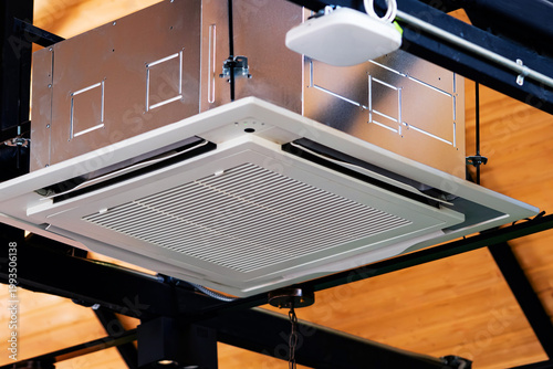 Modern cassette type air conditioner installed on loft ceiling with steel beams and wooden roof. Ceiling-mounted cassette air conditioning unit integrated into modern interior design. HVAC systems.