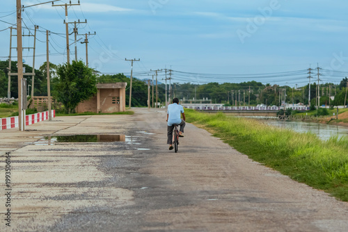 Male cyclist exercise by riding along towpath on a canal. 
People cycle on the dike along meadows and river. Happy and healthy elderly man exercises by cycling on  road alongside irrigation canal.