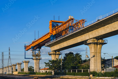 Construction of massive elevated railway viaduct using  gantry crane for girder installation. Elevated railway construction site with heavy machinery and concrete pillars for modernization transit.
