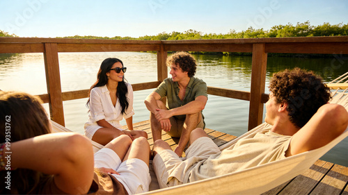 Cheerful young friends sharing a delightful moment on a wooden dock by the serene water, enjoying conversation and a tranquil natural environment together.