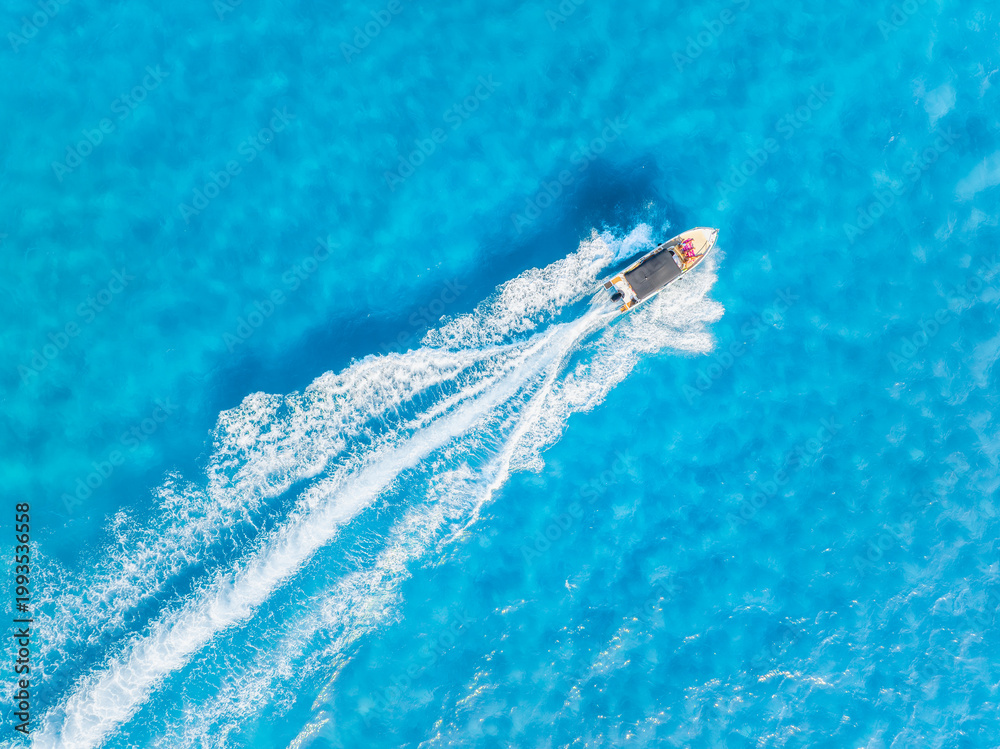 Naklejka premium Aerial top down view of a speed boat cruising through turquoise sea waves. Summer vacation and travel concept. Drone shot of azure ocean water and white foam trail.